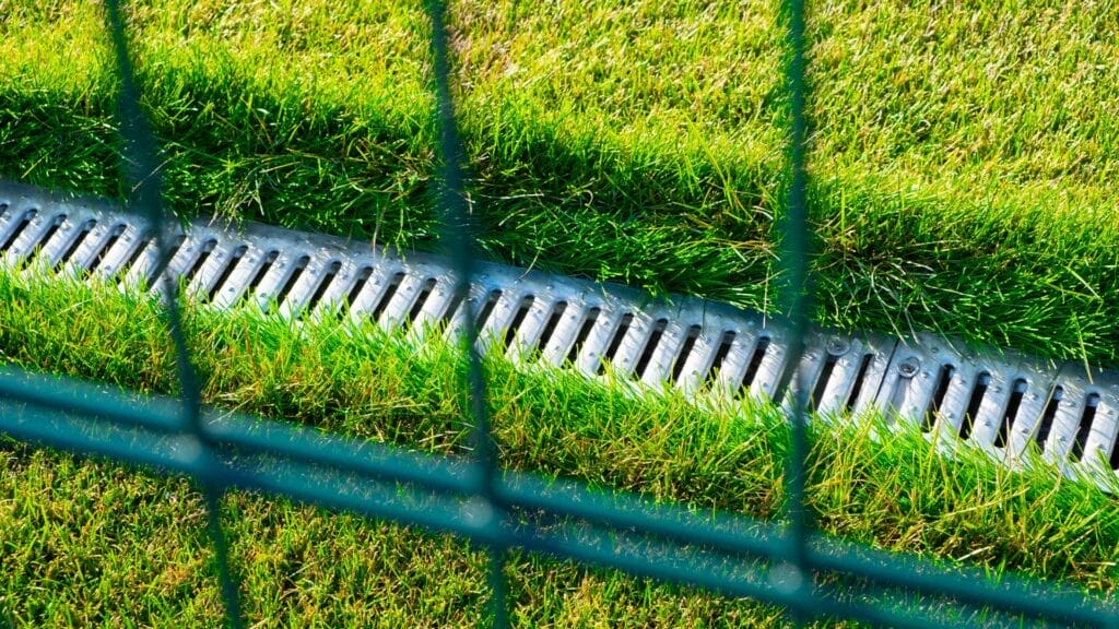 How do you ensure proper drainage on a grass tennis court?