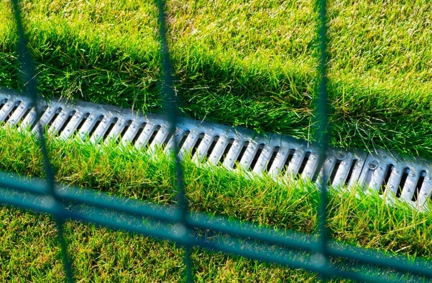How do you ensure proper drainage on a grass tennis court?